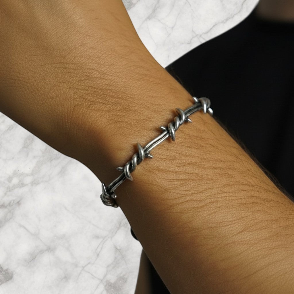 Champion of God silver barbed wire crown of thorns bracelet on a wrist with a tattoo.